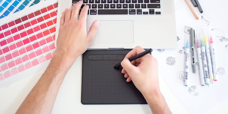 Diseñador trabajando con una tableta gráfica junto a guías de color impresas