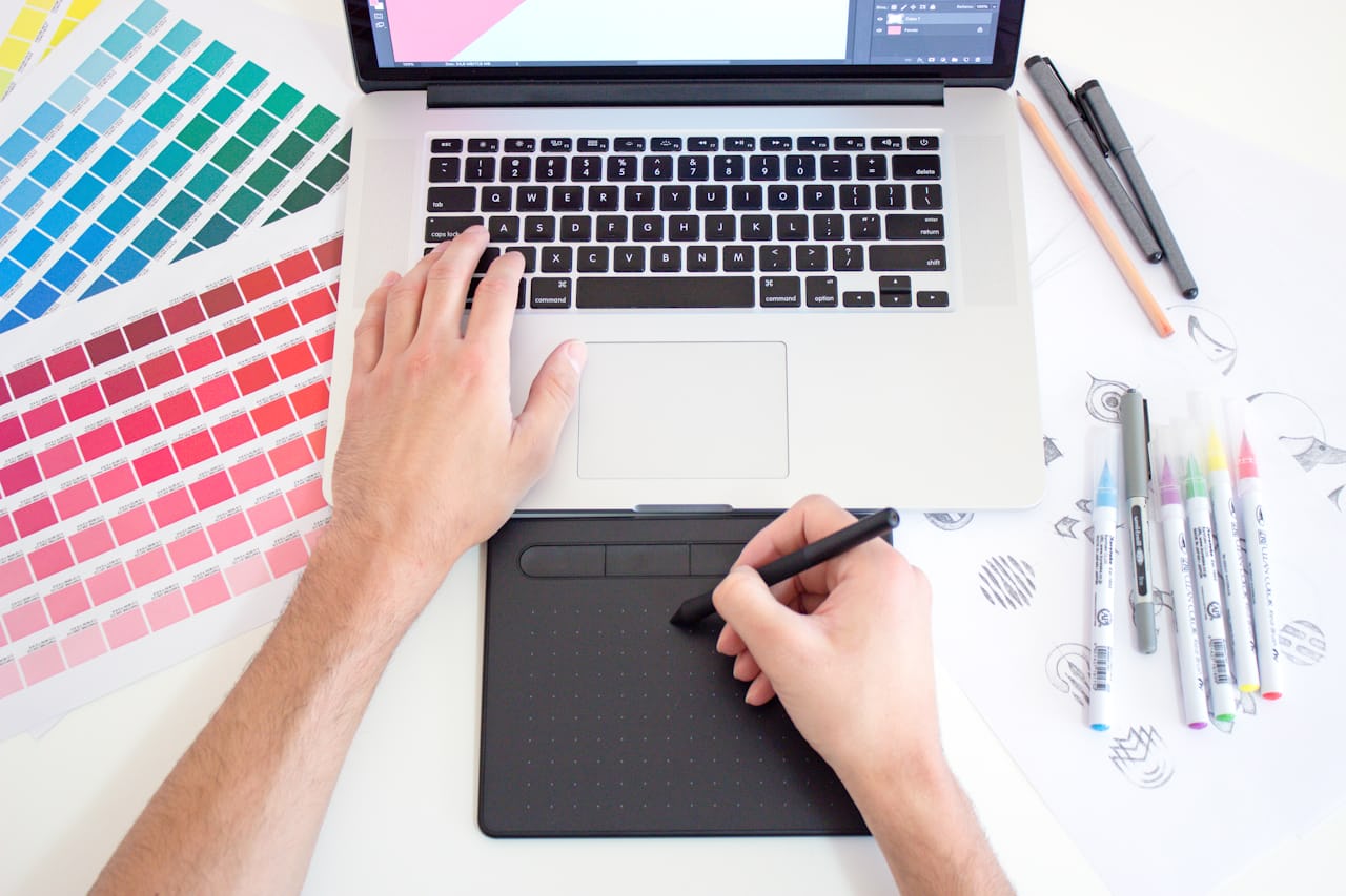Diseñador trabajando con una tableta gráfica junto a guías de color impresas